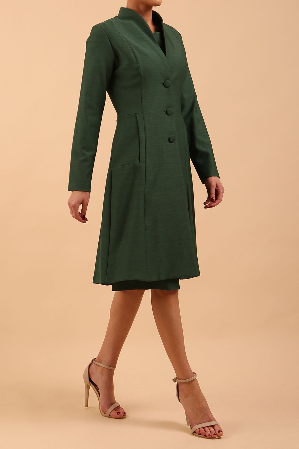 brunette model wearing diva catwalk couture fine raquella coat with buttons across the front and long sleeves with high neck and pockets in chrome green colour front side