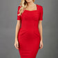 blonde model wearing seed belgravia square neckline red pencil dress with short pleated sleeves and folded pleating like corset band  at the front 