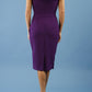 brunette model wearing diva catwalk evening pencil skirt dress sleeveless with lowered neckline and pleating on side in passion purple colour backl