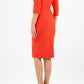 A model is wearing a three quarter sleeve pencil dress with a round neckline and bow detail at the front in orange back image
