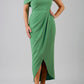 blonde model wearing diva catwalk vegas calf length emerald green midaxi dress with wide bardot neckline and open shoulders with a large opening at the front of the skirt with pleating coming down long skirt front