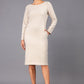 brunette model wearing diva catwalk cora white pencil dress with long sleeves and rounded neckline with pockets in colour sandy cream on side front