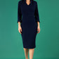 brunette model wearing diva catwalk adriana pencil dress with low v-neck and pleating around shoulders with three quarter sleeve detailed on end and wide waistband in navy front