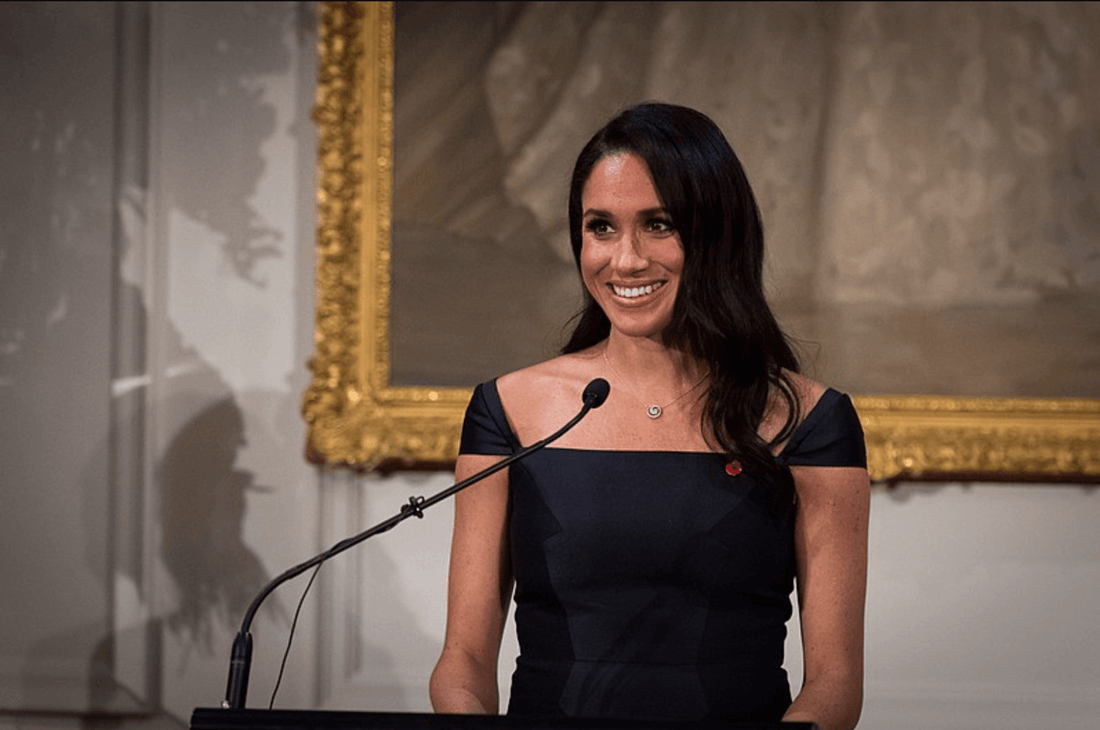 Meghan Markle giving a speech in a black boat neck dress