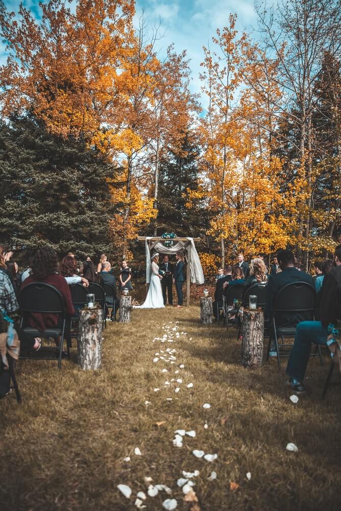 couple getting married outside with background of trees with autumn colours 