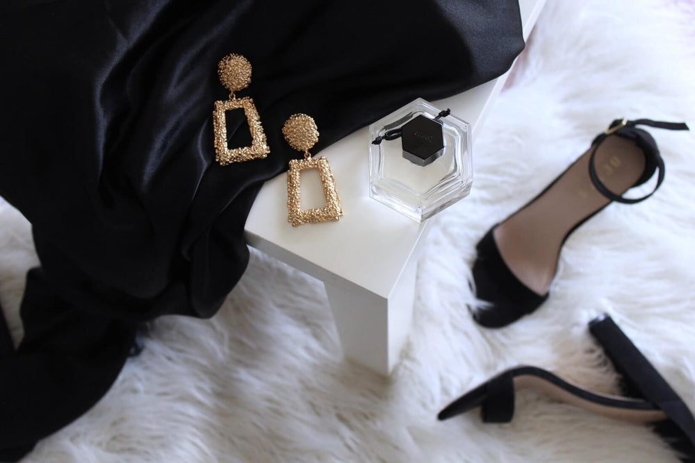 photo of black shoes on a white carpet with gold earrings