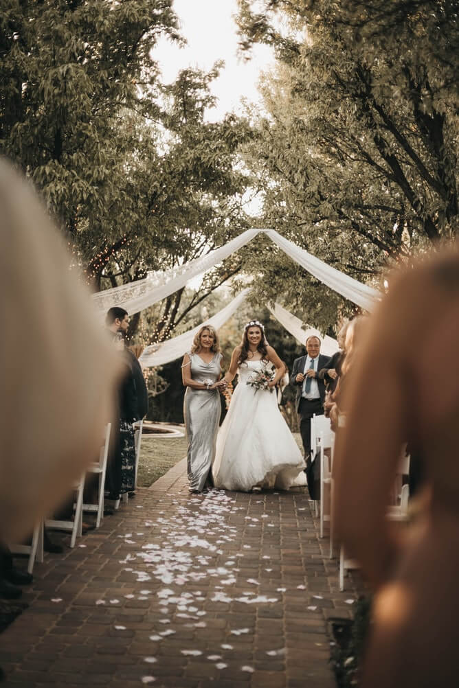 mother in mother of the bride dresses walking her daughter down the aisle 