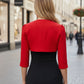 A woman wearing a red cropped bolero jacket with 3/4 sleeves and black clothing underneath. BACK