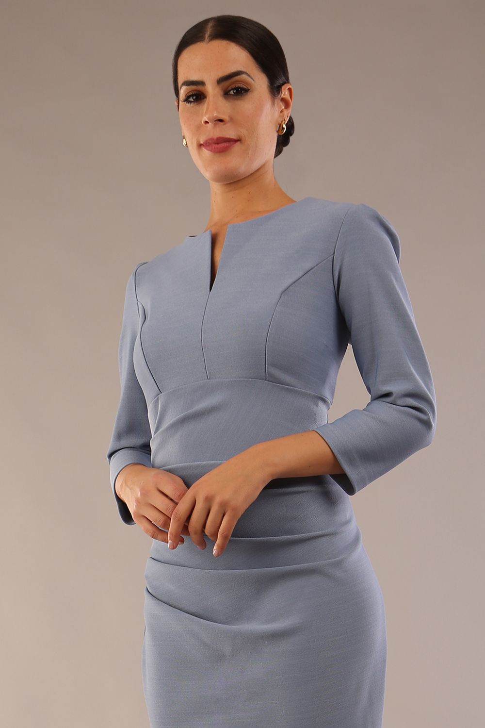 model is wearing a diva catwalk seed fitzrovia 3/4 sleeve pencil dress with round neckline and v-slit and pleating details on the skirt in steel blue front