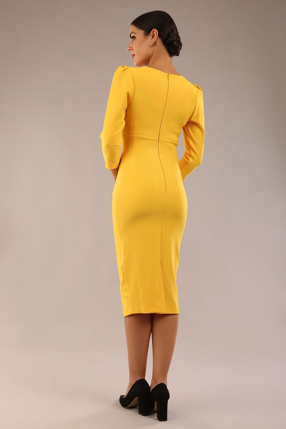 model is wearing A diva catwalk seed fitzrovia 3/4 sleeve pencil dress with round neckline and v-slit and pleating details on the skirt in daffodil yellow back