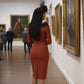model is wearing diva catwalk pencil dress with contrasting asymmetric satin neckline in marsala brown front with black accents standing in an art gallery.