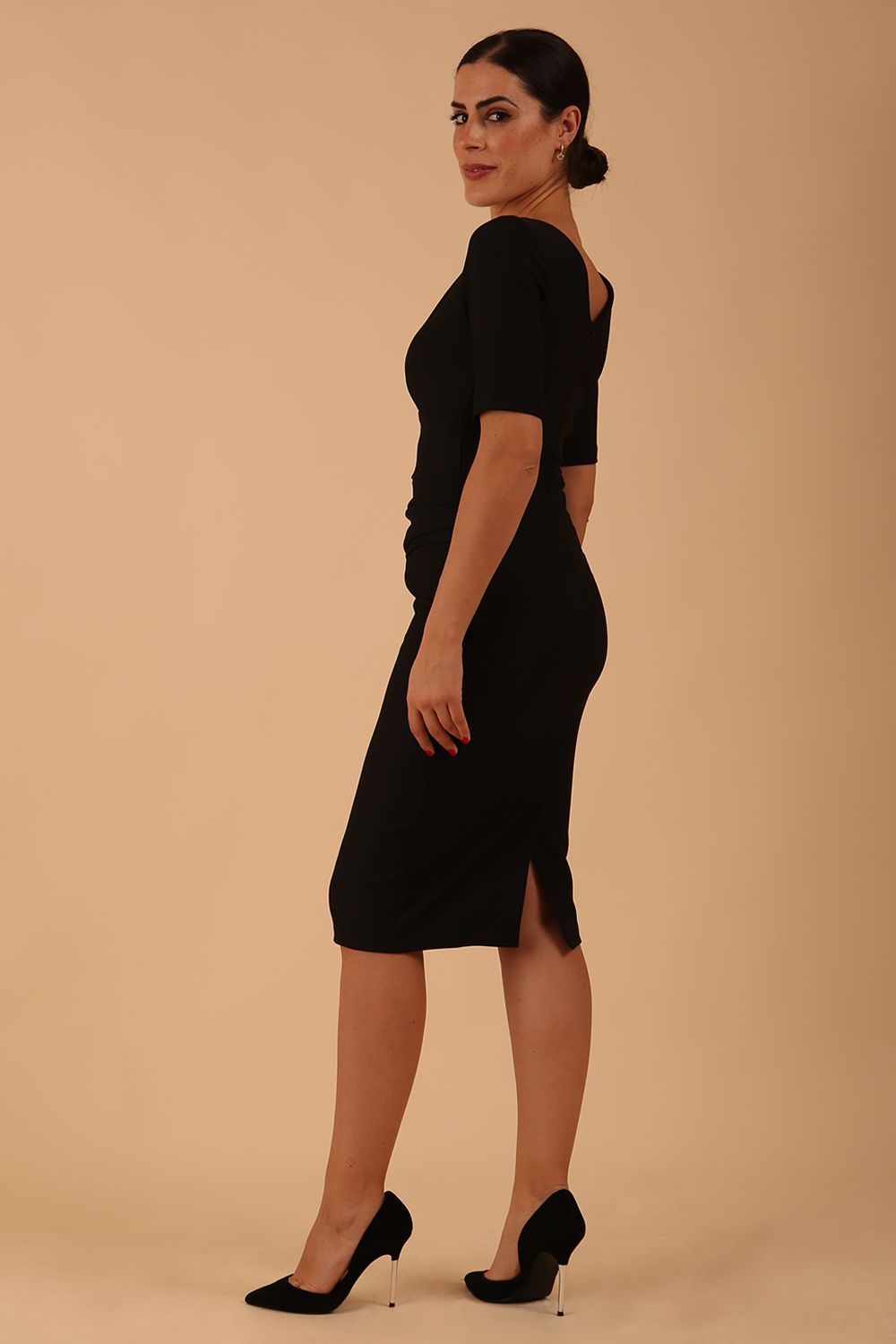 model wearing diva catwalk couture wiltshire fitted pencil-skirt dress with short sleeves and open v-neckline and pleating across the tummy area in black colour front
