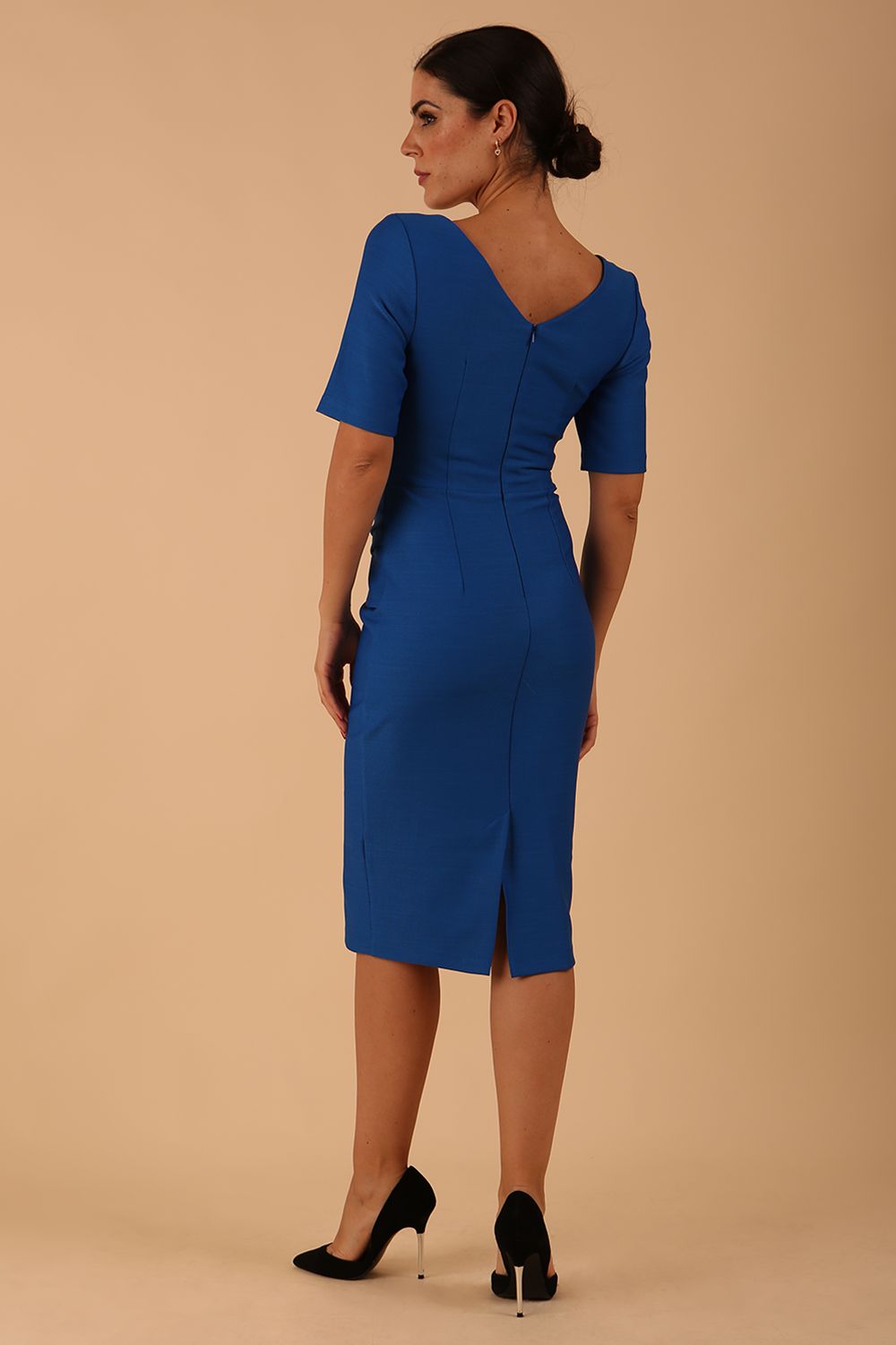 model wearing diva catwalk couture wiltshire fitted pencil-skirt dress with short sleeves and open v-neckline and pleating across the tummy area in sapphire blue colour back