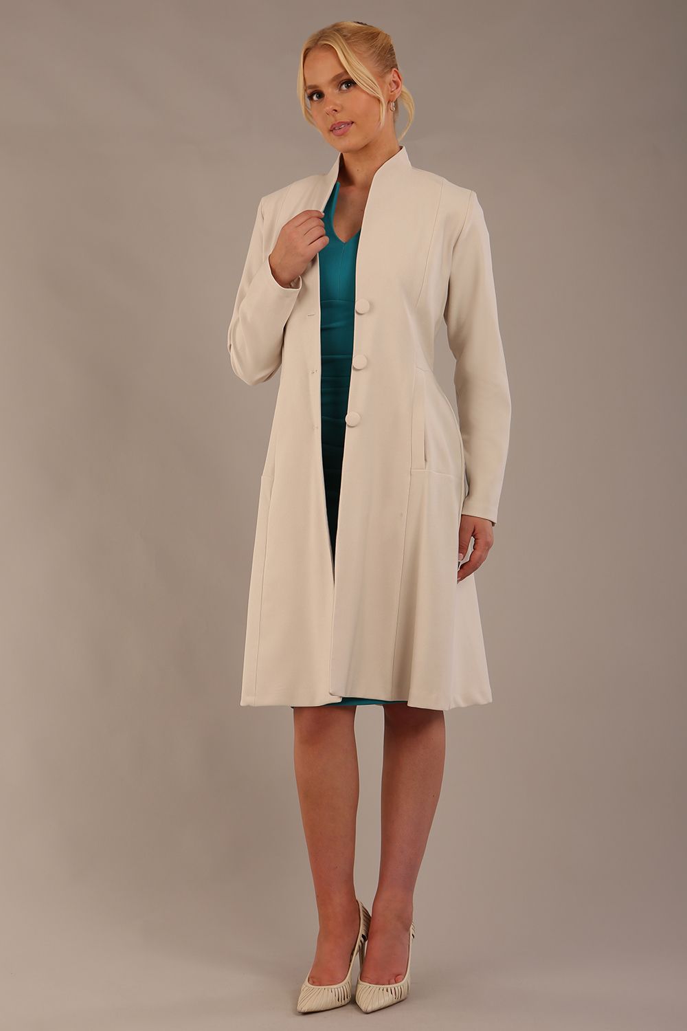 blonde model wearing diva catwalk couture fine raquella coat with buttons across the front and long sleeves with high neck and pockets in sandy cream colour front (Sandy Cream)