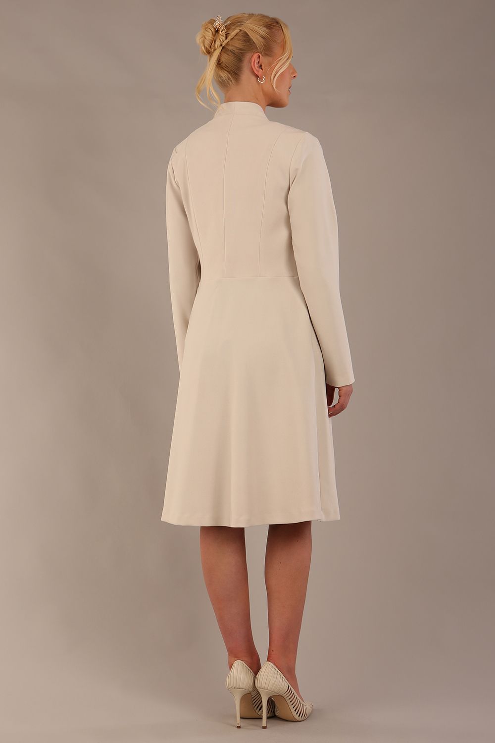 blonde model wearing diva catwalk couture fine raquella coat with buttons across the front and long sleeves with high neck and pockets in sandy cream colour back (Sandy Cream)