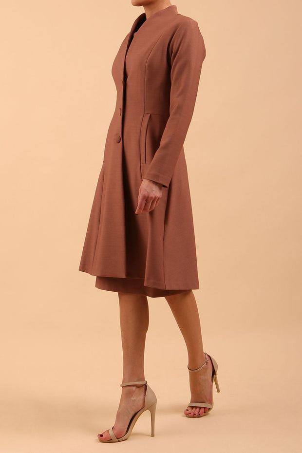  model wearing diva catwalk couture fine raquella coat with buttons across the front and long sleeves with high neck and pockets in acorn brown colour front