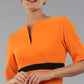 brunette model wearing diva catwalk nadia fitted dress with pencil pleated skirt with sleeves and rounded neckline with split in colour sun orange front