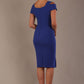Woman wearing a riviera blue diva catwalk hayward pencil dress with short sleeves against a beige background back view