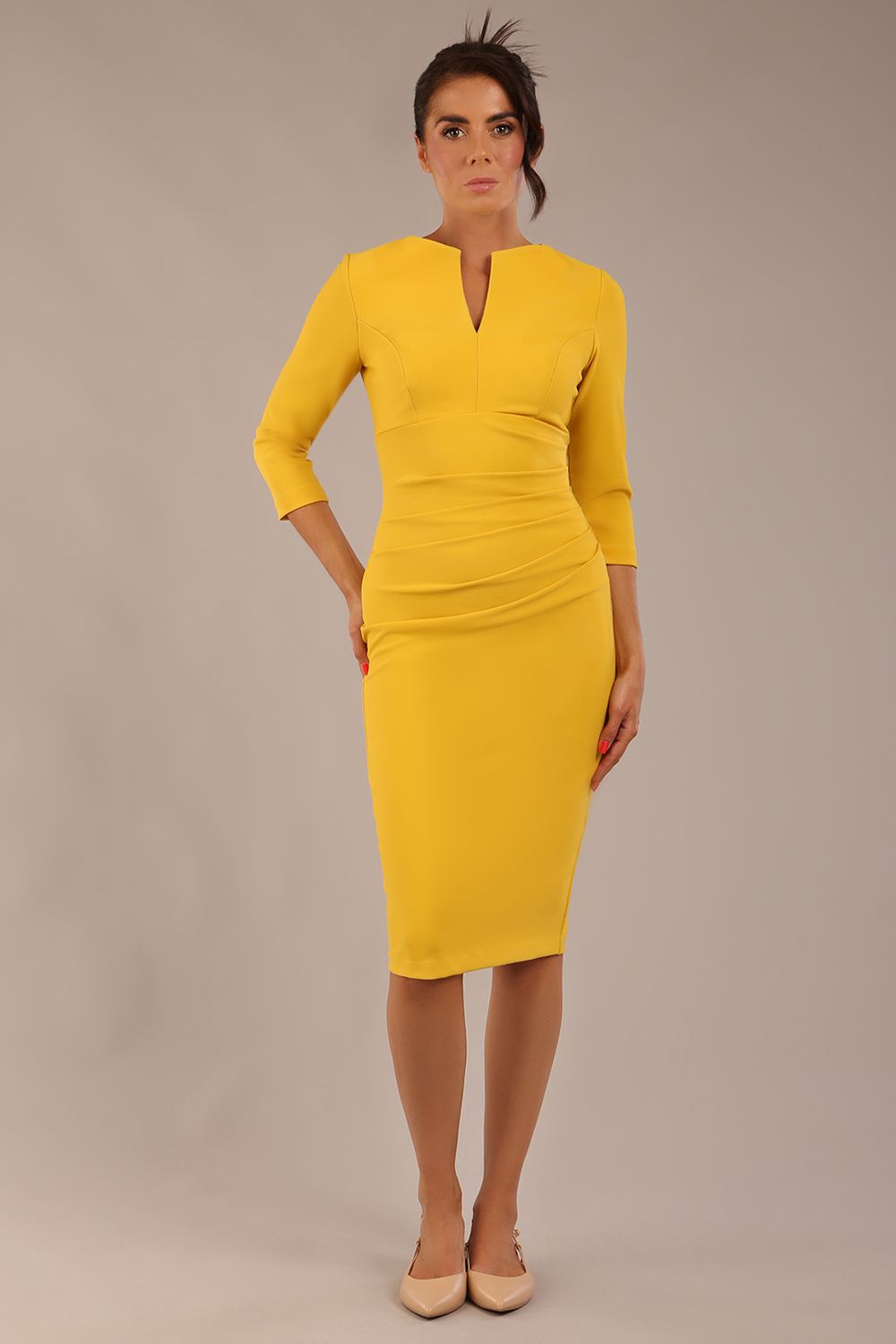 brunette model wearing diva catwalk best selling lydia pencil sleeved dress with slit at the neckline and pleating across the tummy in colour mustard yellow front