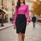 Woman in a pink top and black skirt walking on a city street.