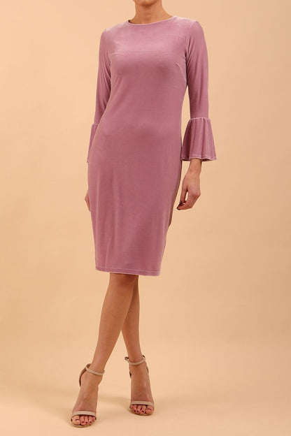 A brunette model is wearing a velvet long bell sleeve pencil dress maternity style in orchid haze colour front