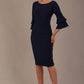 A woman wearing a navy blue knee-length diva catwalk meridian pencil dress with a round neckline, double layered peplum three quarter length sleeves, and standing against a plain background.