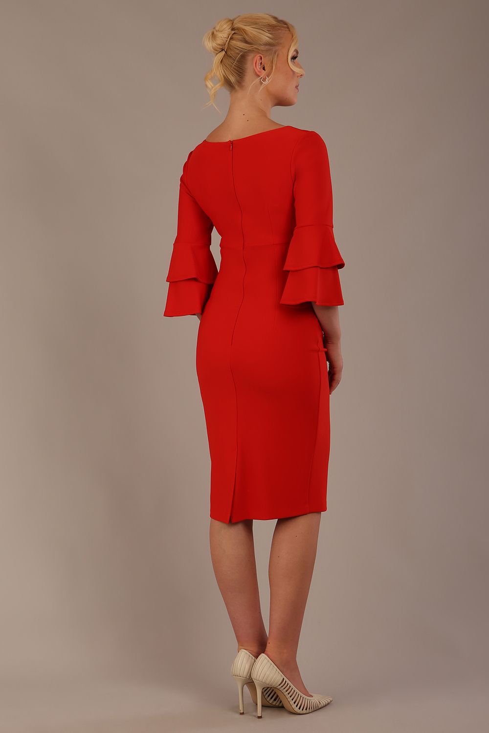 A woman wearing a burnt orange knee-length diva catwalk meridian pencil dress with a round neckline, double layered peplum three quarter length sleeves, and standing against a plain background.