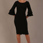 A woman wearing a black knee-length diva catwalk meridian pencil dress with a round neckline, double layered peplum three quarter length sleeves, and standing against a plain background.