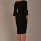A woman wearing a black knee-length diva catwalk meridian pencil dress with a round neckline, double layered peplum three quarter length sleeves, and standing against a plain background back view