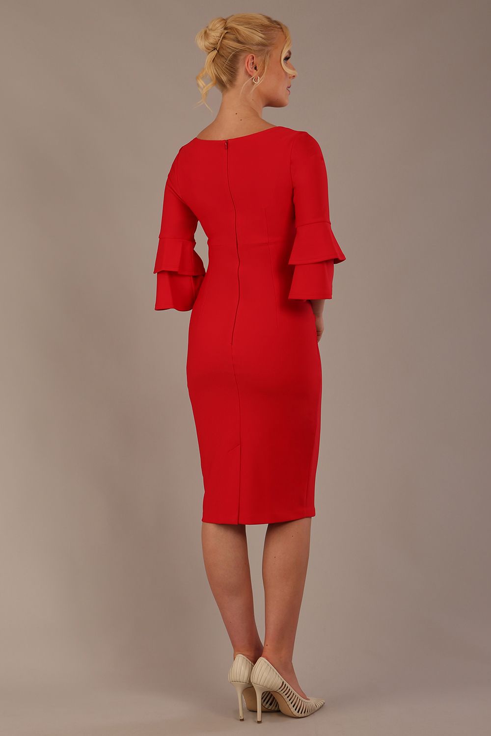 A woman wearing a electric red knee-length diva catwalk meridian pencil dress with a round neckline, double layered peplum three quarter length sleeves, and standing against a plain background back image
