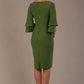A woman wearing a vineyard green knee-length diva catwalk meridian pencil dress with a round neckline, double layered peplum three quarter length sleeves, and standing against a plain background back view