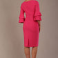 A woman wearing a hibiscus pink knee-length diva catwalk meridian pencil dress with a round neckline, double layered peplum three quarter length sleeves, and standing against a plain background back view