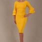 A woman wearing a sunshine yellow knee-length diva catwalk meridian pencil dress with a round neckline, double layered peplum three quarter length sleeves, and standing against a plain background