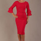 A woman wearing a yarrow pink knee-length diva catwalk meridian pencil dress with a round neckline, double layered peplum three quarter length sleeves, and standing against a plain background.