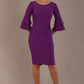 A woman wearing a royal purple knee-length diva catwalk meridian pencil dress with a round neckline, double layered peplum three quarter length sleeves, and standing against a plain background.