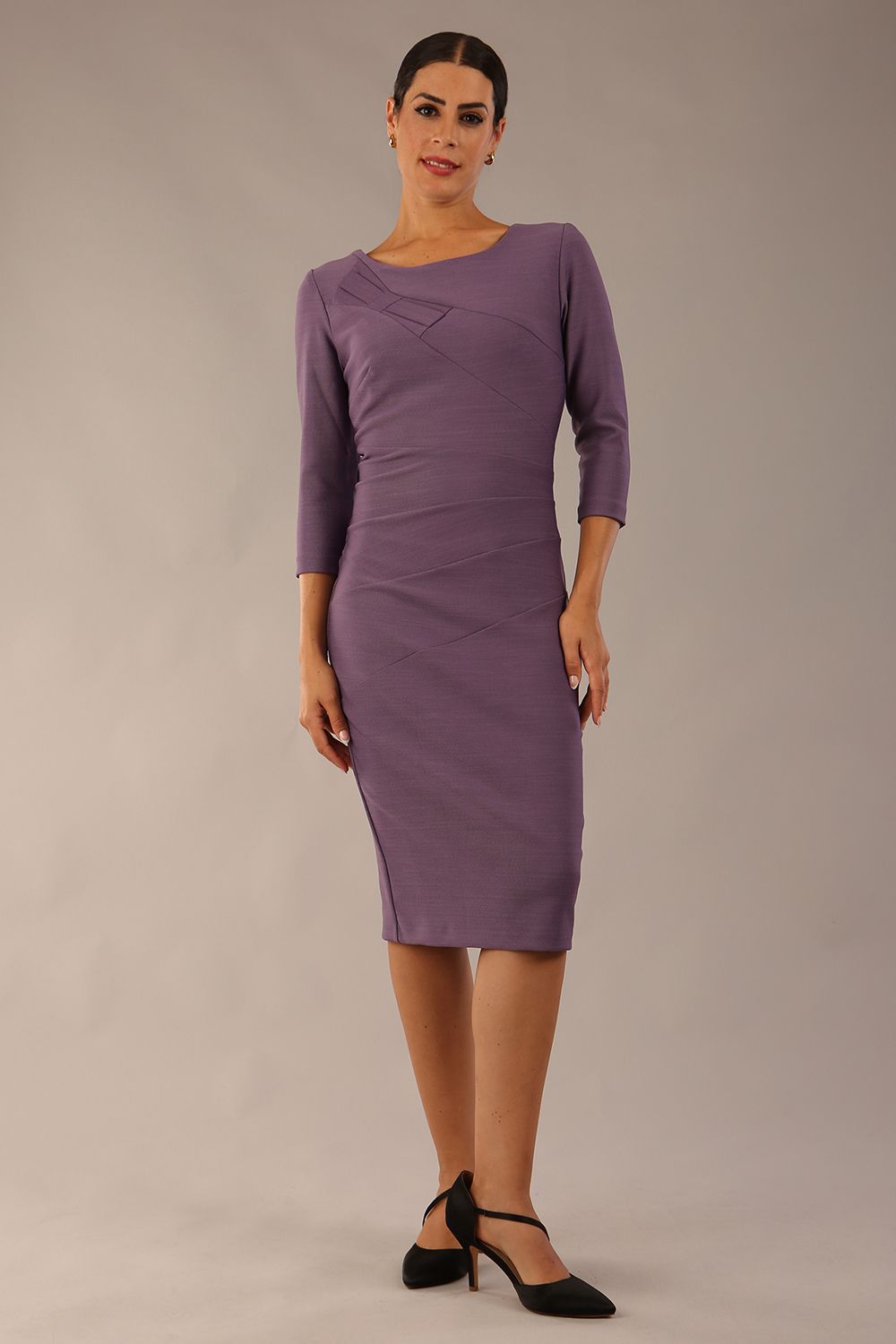 brunette model wearing diva catwalk couture althorp pencil fitted dress with sleeves and rounded neckline and bow detail at the top in dusky lilac colour front