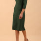 brunette model wearing diva catwalk couture althorp pencil fitted dress with sleeves and rounded neckline and bow detail at the top in chrome green colour front side
