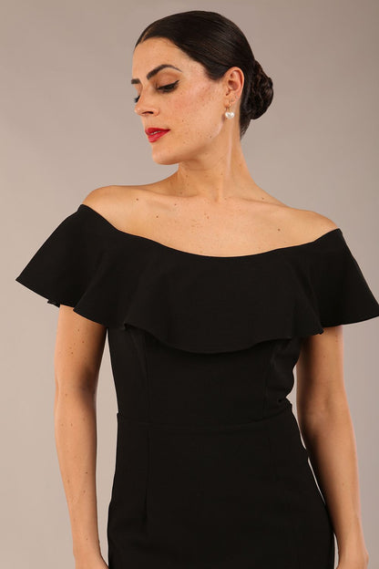 brunette model wearing diva catwalk pencil dress with off shoulder frilled front and bardot neckline in black colour front