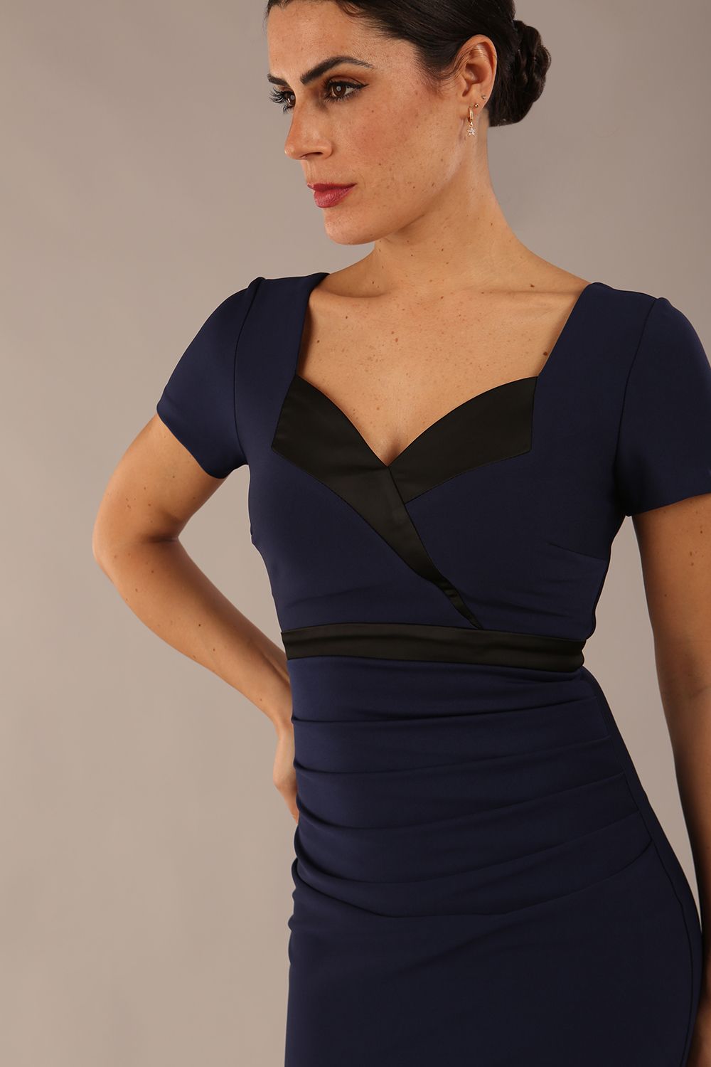 model is wearing a diva catwalk dress in navy blue with black satin detail contrast on the neckline and waistband short sleeves and pleating details with knee length