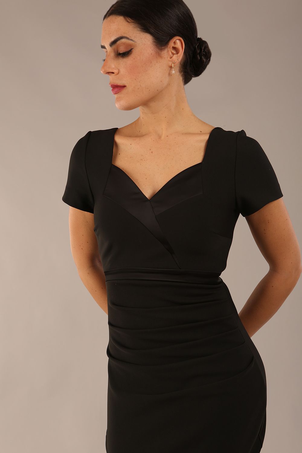 model is wearing a diva catwalk dress in black with black satin detail contrast on the neckline and waistband short sleeves and pleating details with knee length