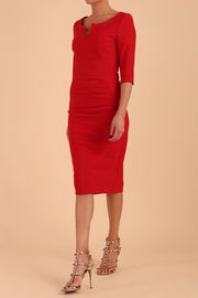 model wearing seed couture royale pencil skirt dress with pleating across the tummy area with rounded neckline with a split in the middle and 3 4 sleeve in Salsa Red colour front side