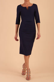 model wearing seed couture royale pencil skirt dress with pleating across the tummy area with rounded neckline with a split in the middle and 3 4 sleeve in Navy Blue colour front