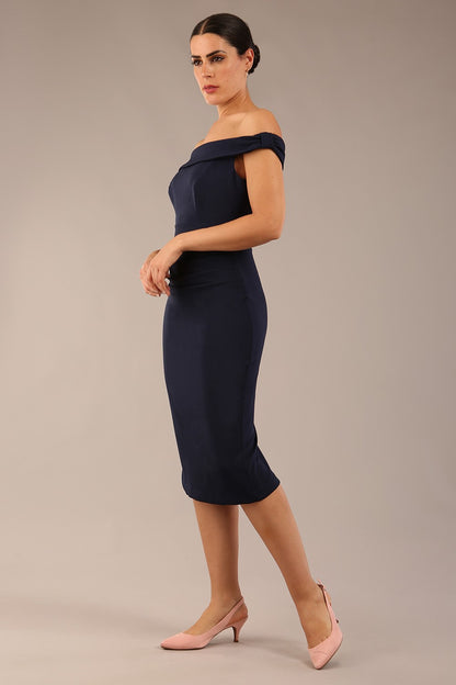 brunette model wearing a diva catwalk cloud pencil fitted flattering dress off shoulder sleeveless with detail with pleating around the front in navy blue front