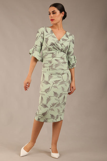 brunette model is wearing a diva catwalk hollie print pencil dress with 3/4 sleeves and frill details v neckline and knee length in deco green fern print front image