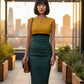 Woman in a print dress wit yellow top and green skirt standing in a vineyard.