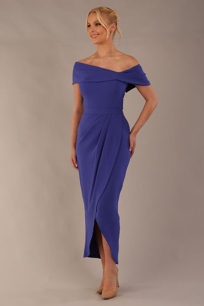 model wearing diva catwalk vegas calf length spectrum indigo midaxi dress with wide bardot neckline and open shoulders with a large opening at the front of the skirt with pleating coming down long skirt front (Spectrum Indigo)