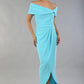 model wearing diva catwalk vegas calf length midaxi dress with wide bardot neckline and open shoulders with a large opening at the front of the skirt with pleating coming down long skirt front in turquoise