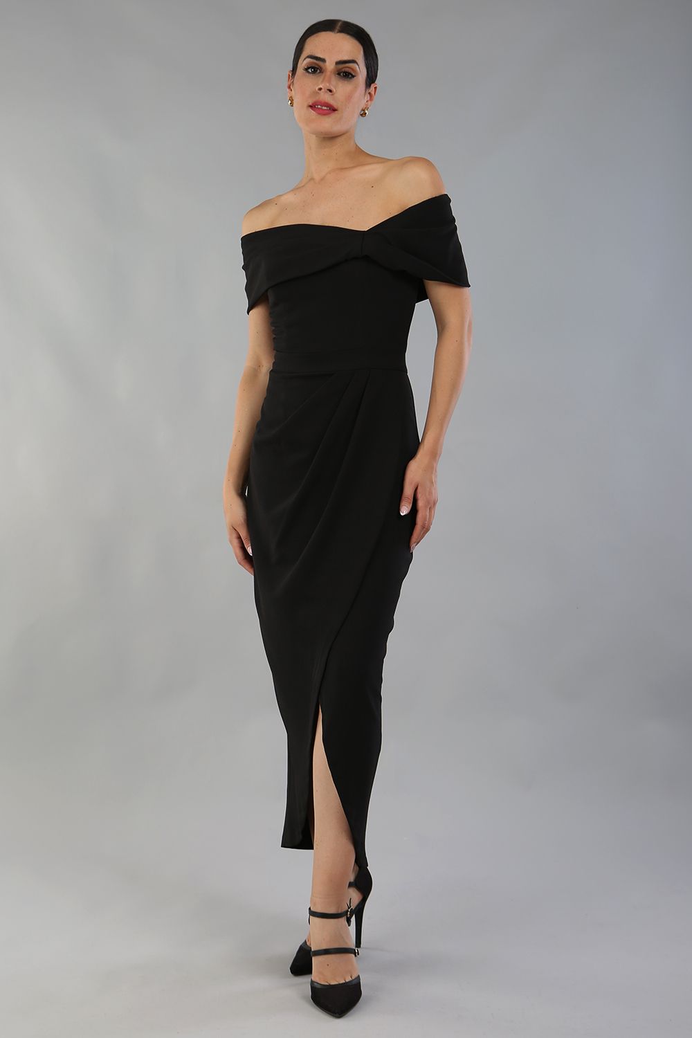 brunette model wearing diva catwalk vegas calf length black midaxi dress with wide bardot neckline and open shoulders with a large opening at the front of the skirt with pleating coming down long skirt front 