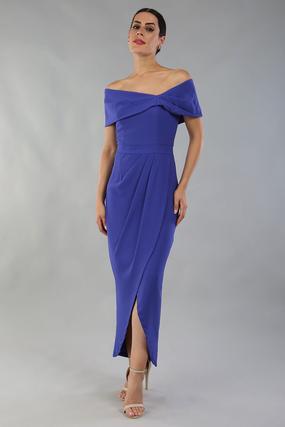 model wearing diva catwalk vegas calf length indigo midaxi dress with wide bardot neckline and open shoulders with a large opening at the front of the skirt with pleating coming down long skirt front