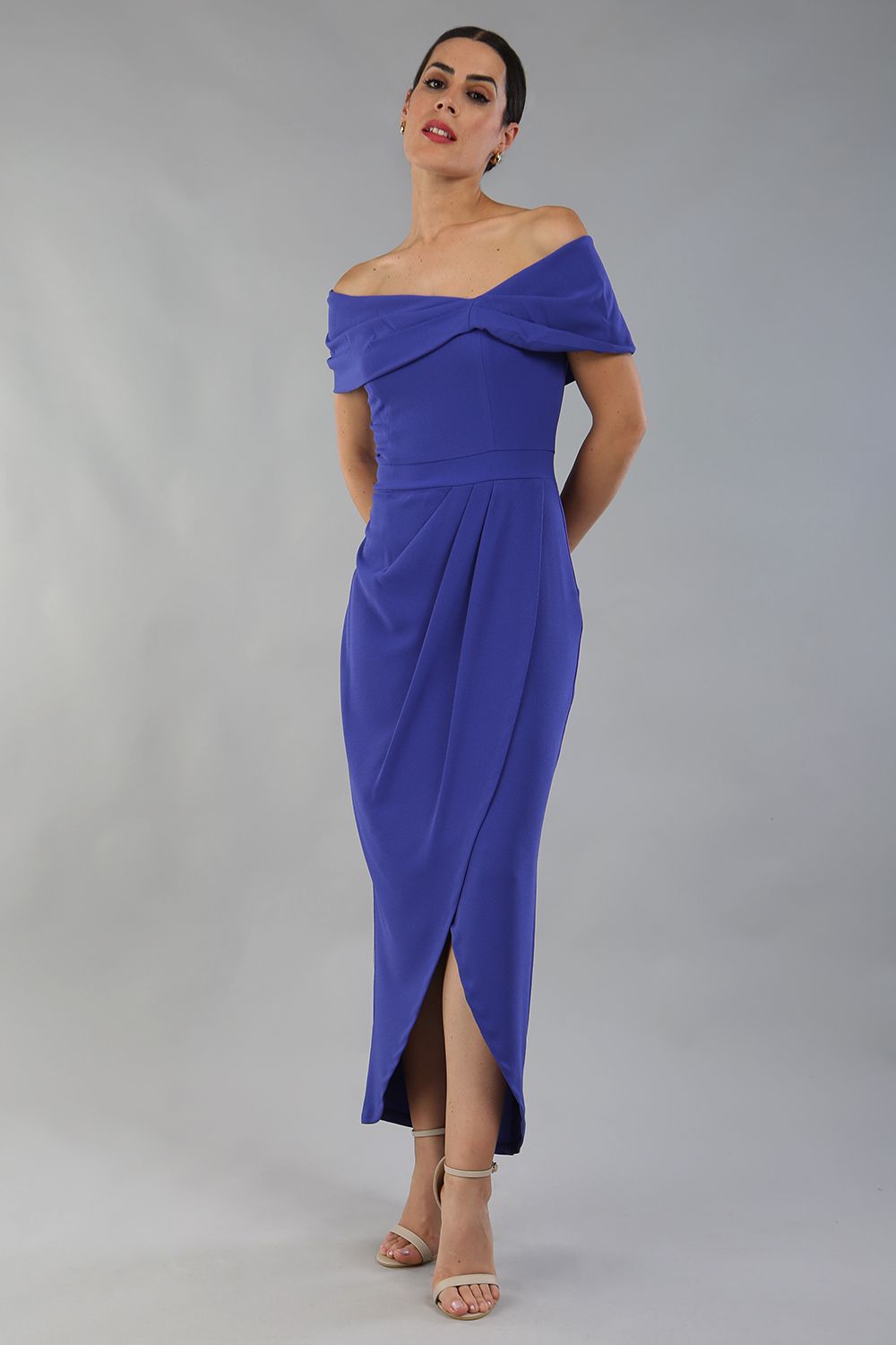 model wearing diva catwalk vegas calf length indigo midaxi dress with wide bardot neckline and open shoulders with a large opening at the front of the skirt with pleating coming down long skirt front